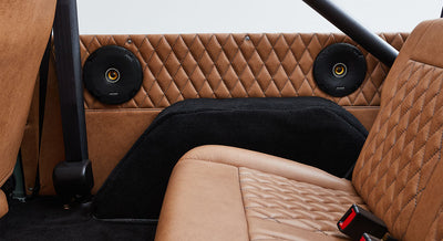 Interior rear passenger area with diamond-stitched tan leather, two black speakers, and black carpeting in Classic Ford