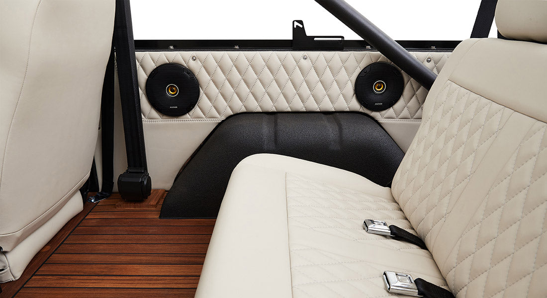 Interior rear side panel of Classic Ford Bronco with two black circular speakers and beige quilted seats