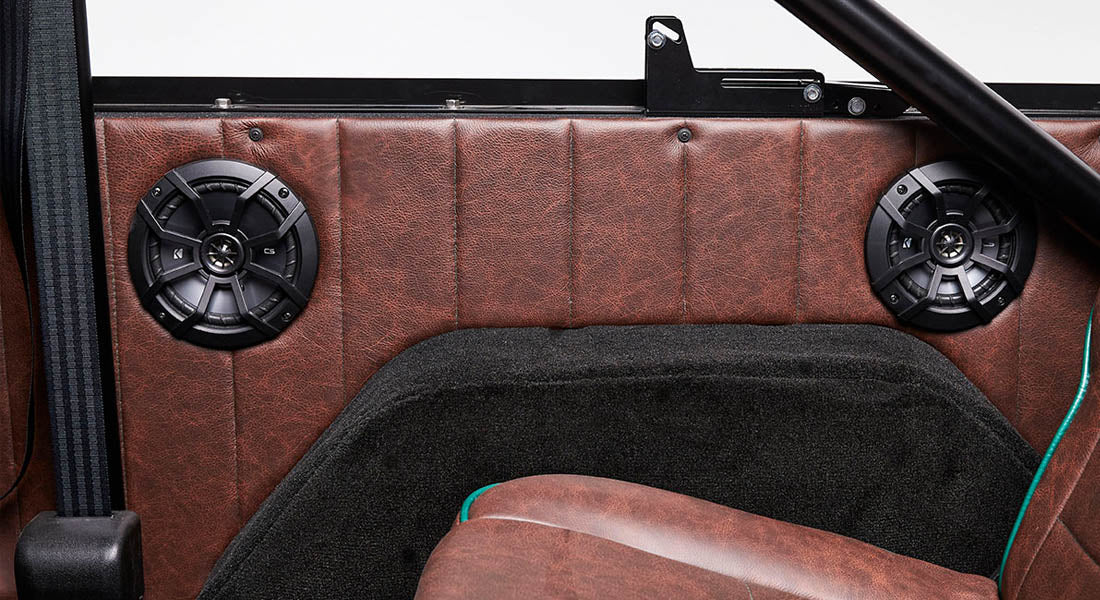 Two black speakers mounted inside Classic Ford Bronco with brown leather interior and black carpeting