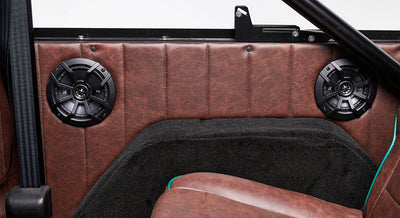 Two black speakers mounted inside Classic Ford Bronco with brown leather interior and black carpeting