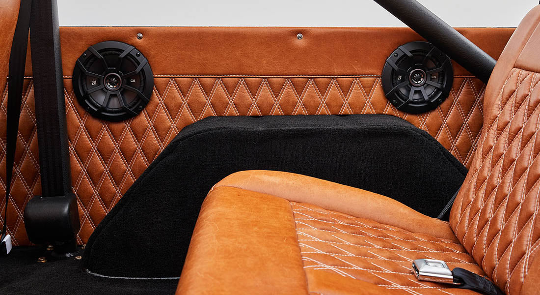 Two black round speakers mounted on caramel brown diamond-stitched leather panel inside vehicle