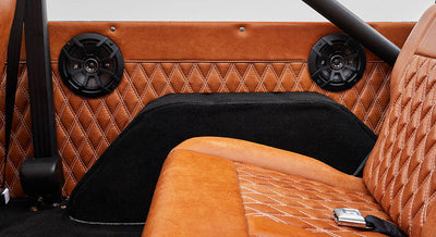 Two black round speakers mounted on caramel brown diamond-stitched leather panel inside vehicle