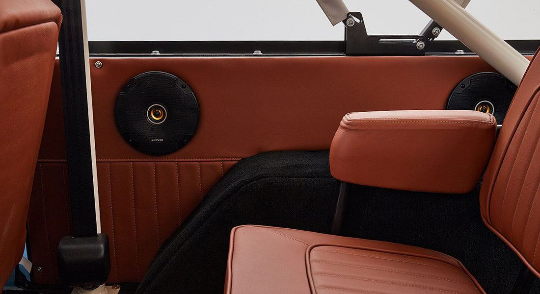 Two black Kicker speakers installed on brown interior panel behind rear seats in Classic Ford Bronco