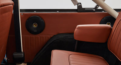 Two black Kicker speakers installed on brown interior panel behind rear seats in Classic Ford Bronco