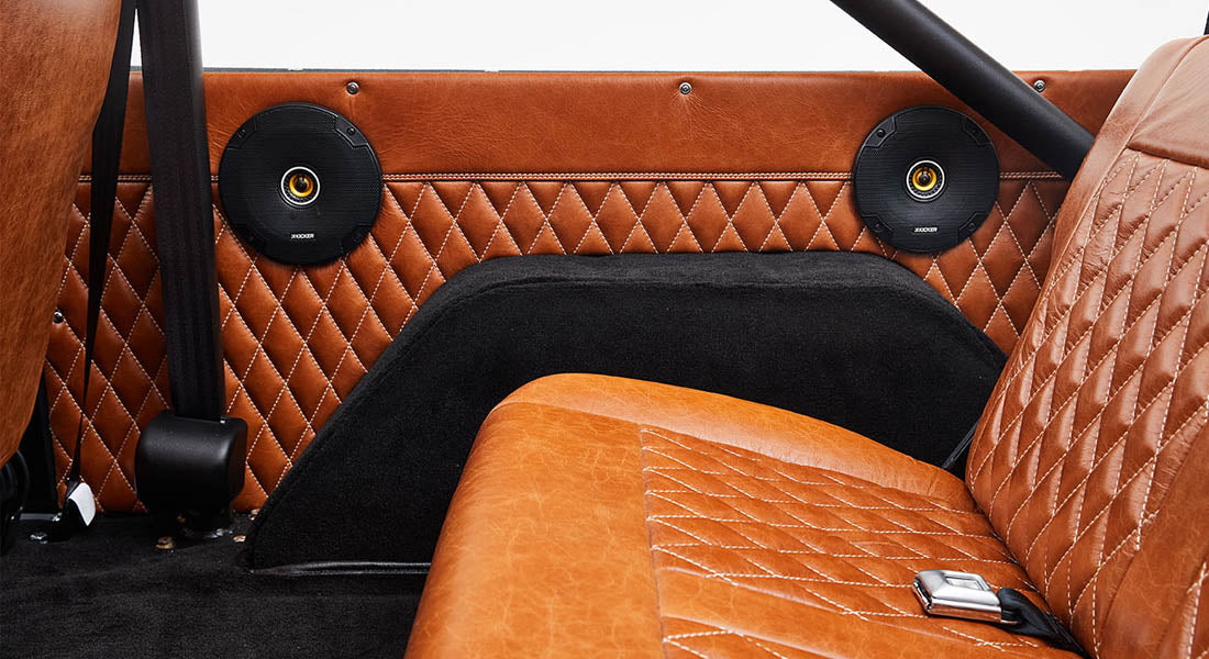Rear interior of Classic Ford Bronco with brown leather quilted door panel and two black speakers