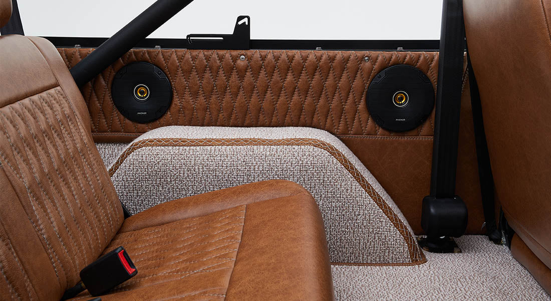 Two round speakers installed in quilted brown leather panels behind rear bench seat in Classic Ford Bronco