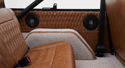 Two round speakers installed in quilted brown leather panels behind rear bench seat in Classic Ford Bronco