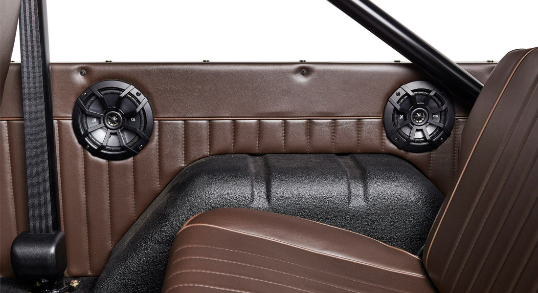 Interior side panel of a Classic Ford Bronco with two black round speakers and brown upholstery.