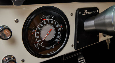 Classic Ford Bronco dashboard speedometer and ignition area with "Bronco" emblem on the steering column panel.