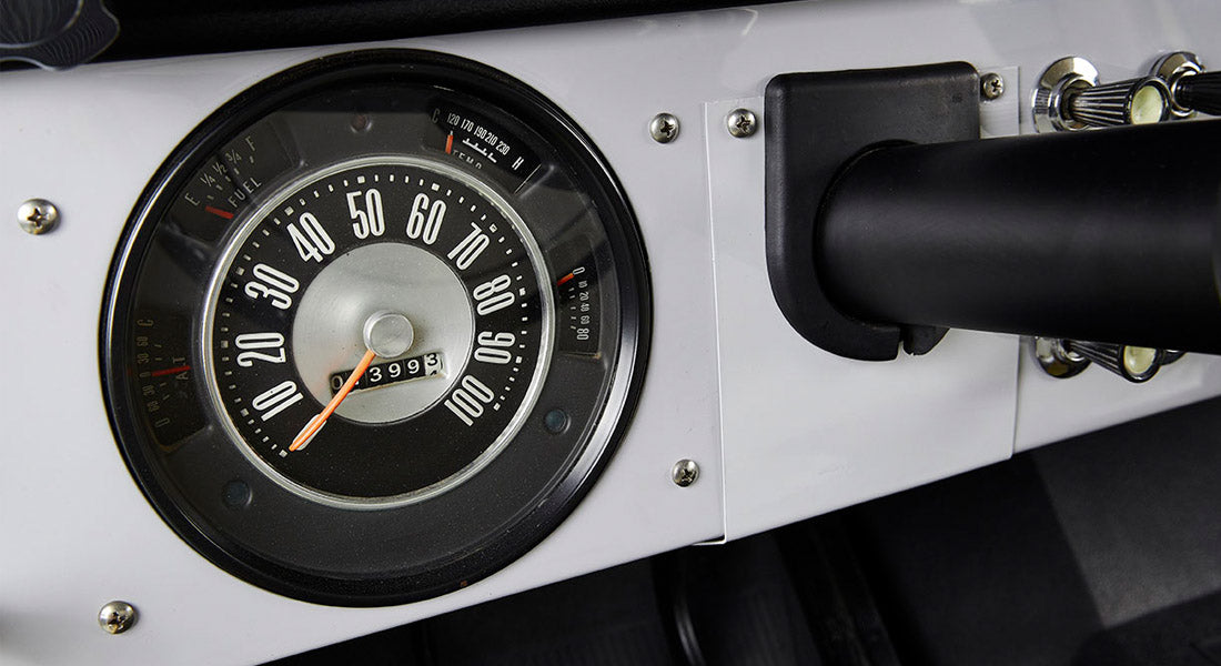 Classic Ford Bronco round speedometer with white numbers and orange needle on white dashboard