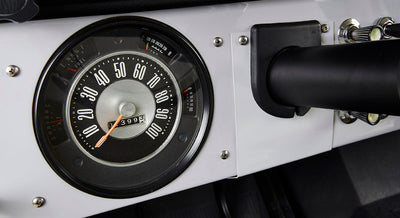 Classic Ford Bronco round speedometer with white numbers and orange needle on white dashboard