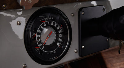 Classic Ford Bronco speedometer with red needle and chrome bezel on a gray dashboard