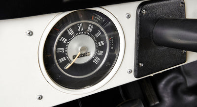 Classic Ford Bronco round speedometer with white numbers and orange needle on white dashboard