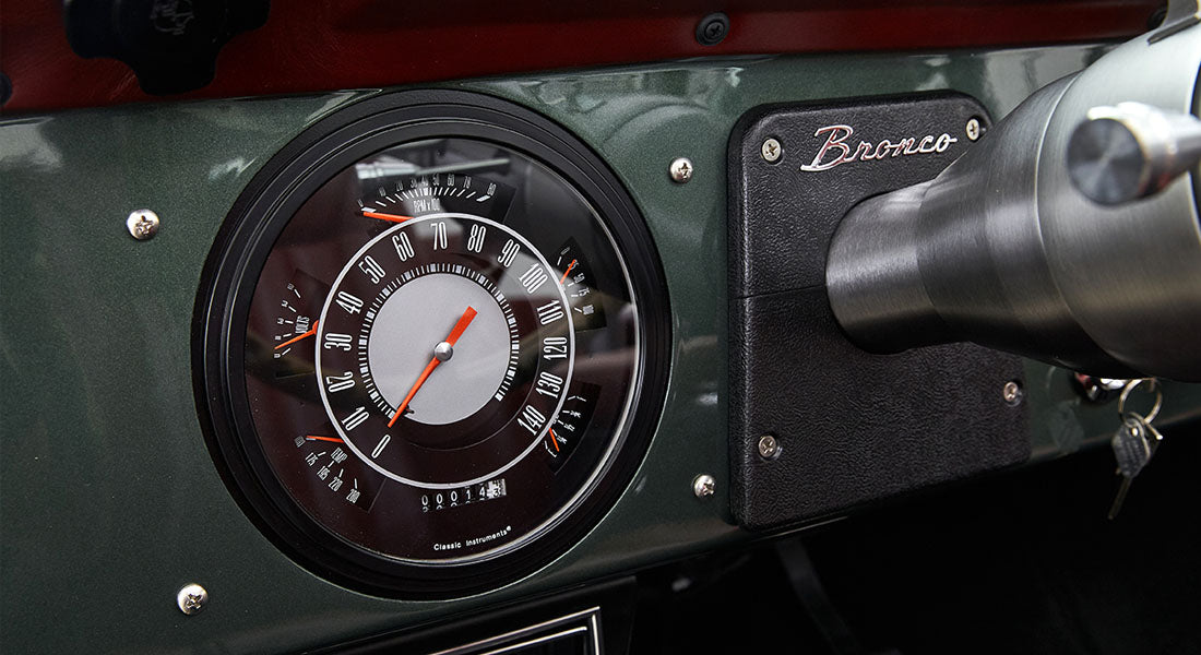 Classic Ford Bronco dashboard with speedometer and Bronco badge on dark green panel