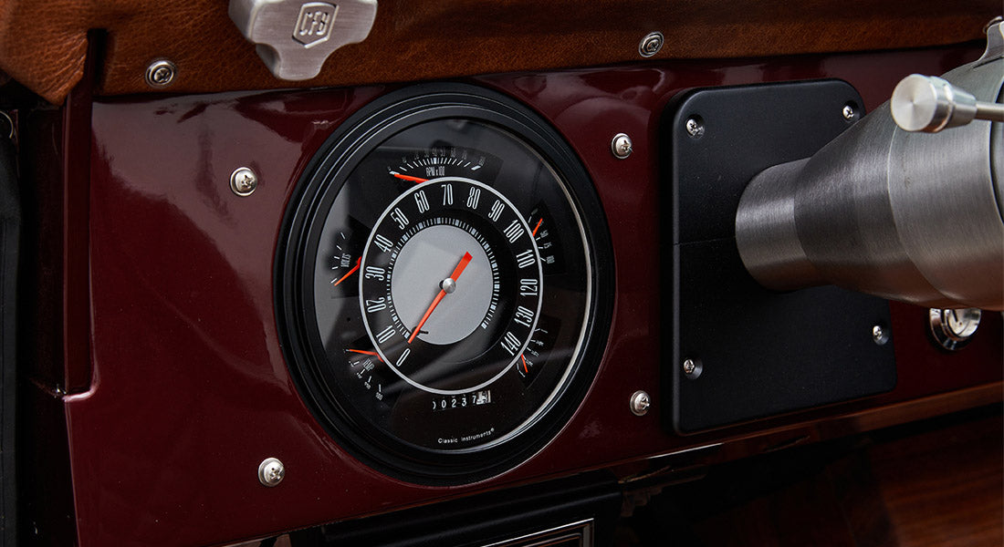 Round speedometer with black and gray face set in deep red dashboard of Classic Ford Bronco