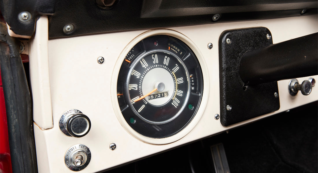 Classic Ford Bronco dashboard showing speedometer gauge and control knobs in black and white interior.