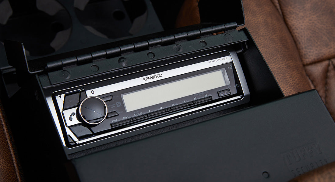 Kenwood stereo unit inside a compartment with a black leather seat visible nearby in a Classic Ford Bronco