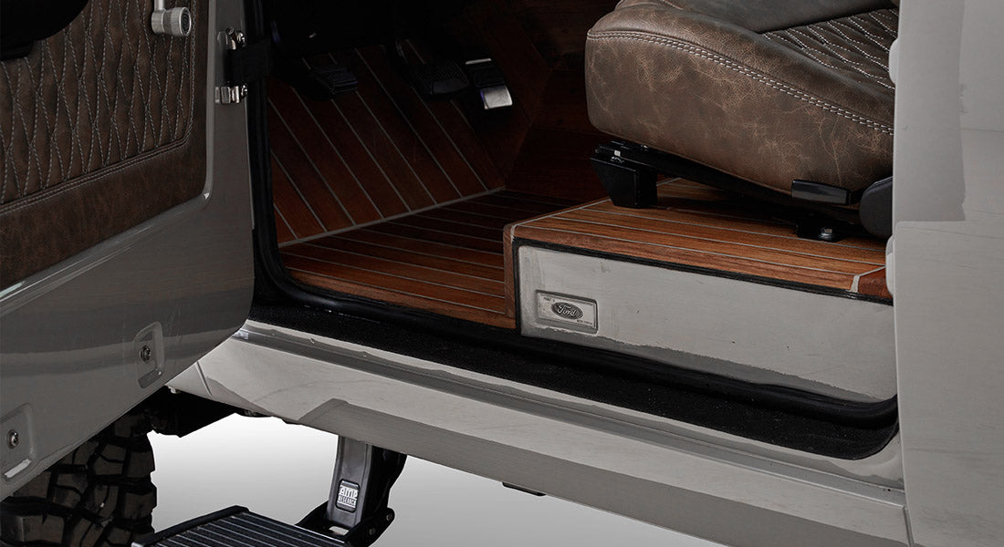 Open vehicle door showing detailed teak wood flooring and brown leather seat