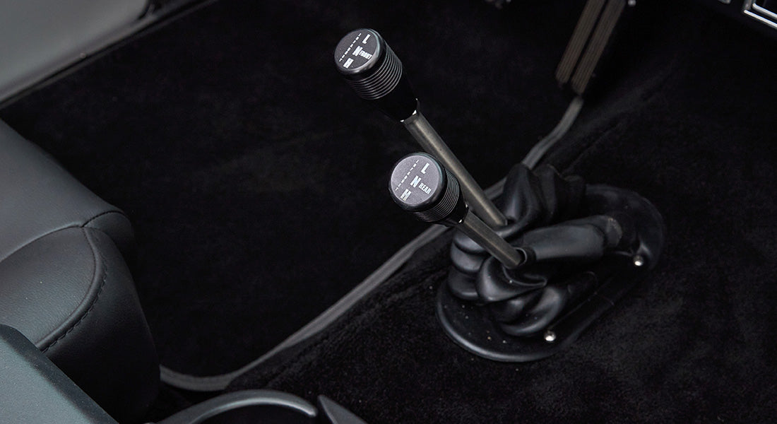 Two gear shift levers on black carpeted floor of Classic Ford Bronco interior