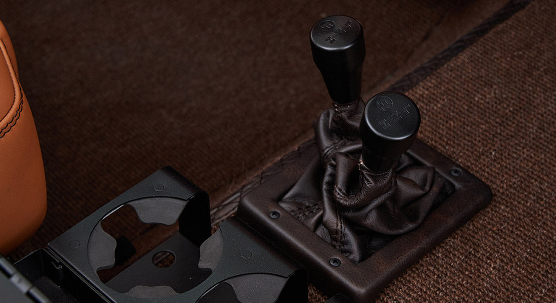 Two black gear shift levers with leather boots and cup holder in Classic Ford Bronco interior