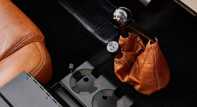 Two black gear shift levers with caramel leather boots and cup holders near driver seat