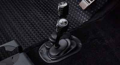 Two black transfer case shifters with white markings on a black rubber floor mat