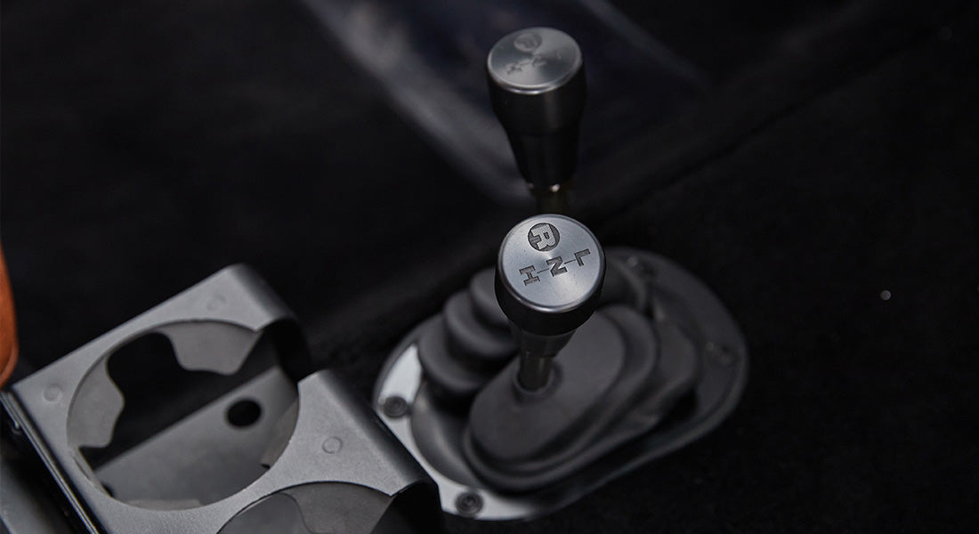 Two gear shifters with black knobs mounted on black carpeted floor