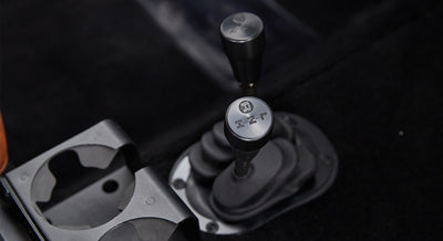 Two gear shifters with black knobs mounted on black carpeted floor