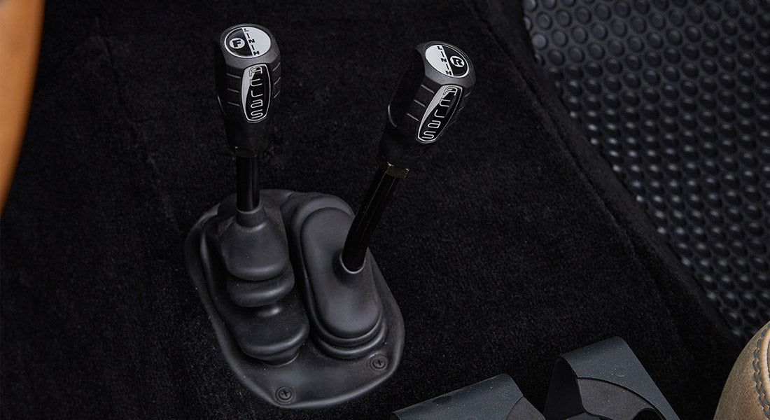 Two black transfer case shifters labeled Aellas with white icons on black carpet