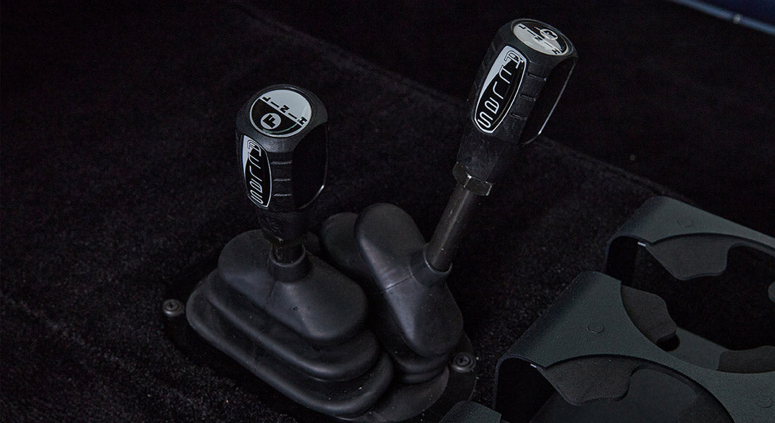 Close-up of two black gear shifters with labels on black carpeted floor with cup holders