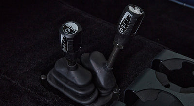 Close-up of two black gear shifters with labels on black carpeted floor with cup holders