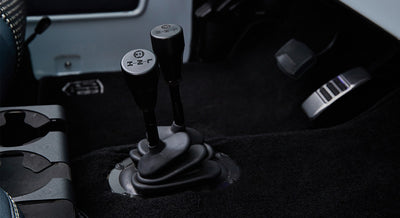 Two black transfer case gear shift levers mounted on black carpeted floor of vehicle interior
