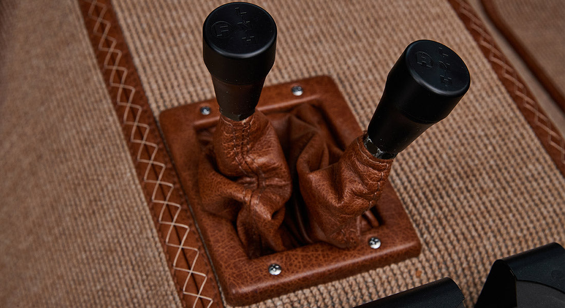Two black gear shift knobs with leather covers on tan carpet floor of Classic Ford Bronco interior