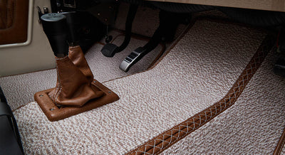 Floor area with gear shift lever covered in brown leather and beige carpet with brown quilted trim