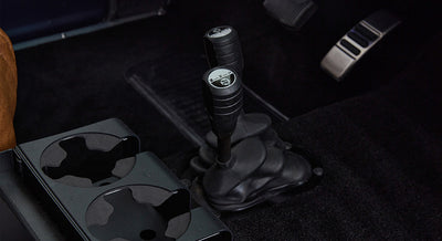 Two black gear shifters and cup holders on black carpeted vehicle floor