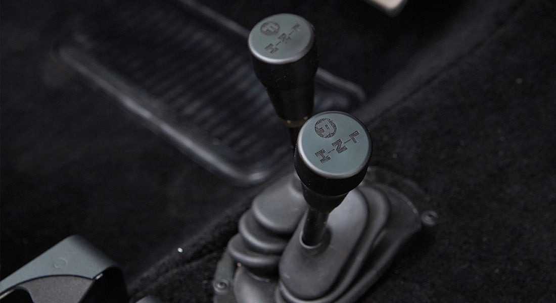 Two black transfer case shift levers installed on black carpeted floor of Classic Ford Bronco interior.