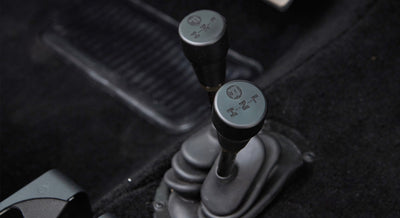 Two black transfer case shift levers installed on black carpeted floor of Classic Ford Bronco interior.