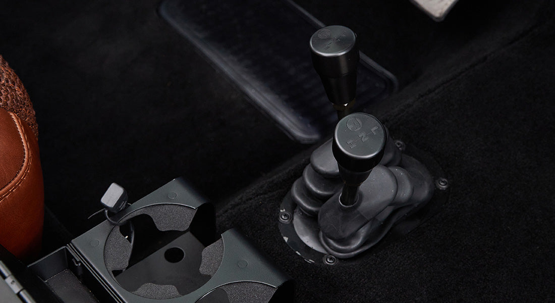 Gear shift levers and cup holders on carpeted floor of Classic Ford Bronco interior.