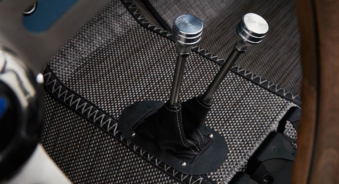 Close-up of two metal transfer case levers with black leather boots surrounded by patterned flooring inside classic Ford