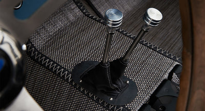 Close-up of two metal transfer case levers with black leather boots surrounded by patterned flooring inside classic Ford