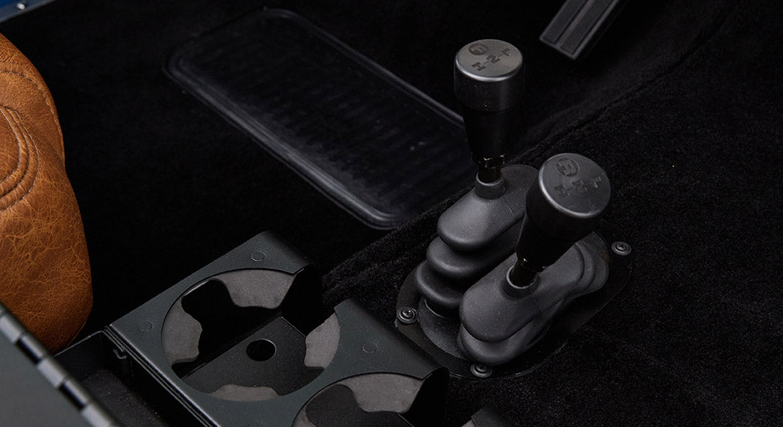 Two gear shifters and cup holders on carpeted floor inside a Classic Ford Bronco