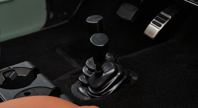 Two black gear shift levers with shift pattern markings on the floor of a Classic Ford Bronco interior.