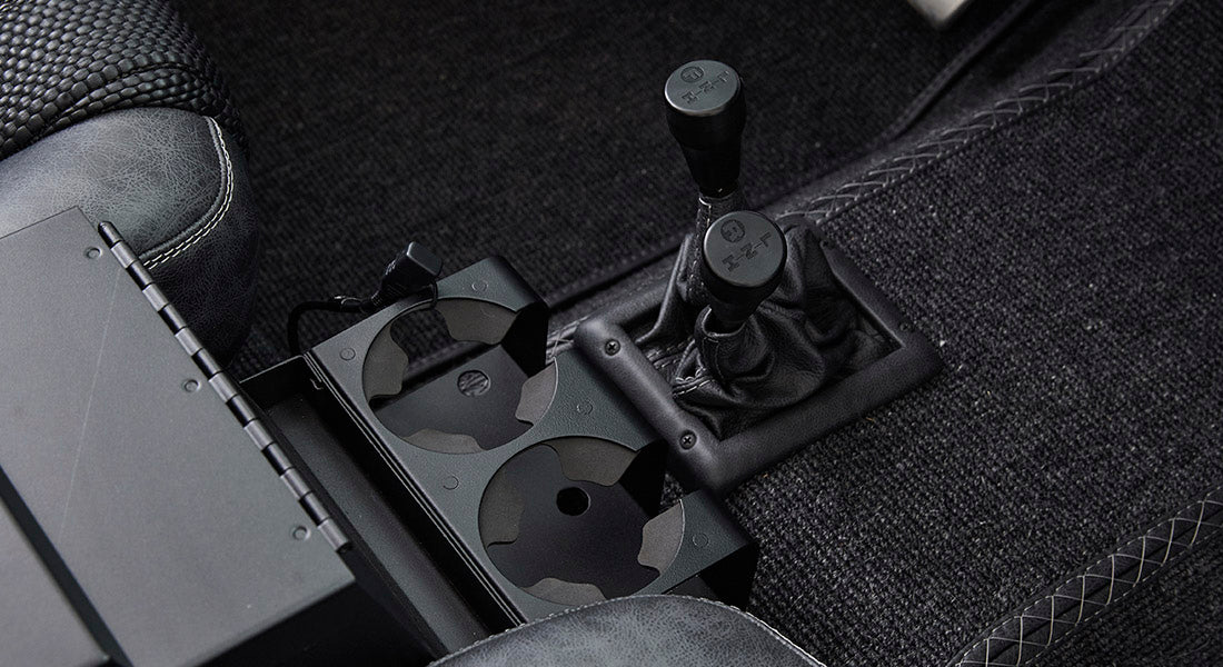 Center console of Classic Ford Bronco with two gear shifters and black cup holders between front seats.