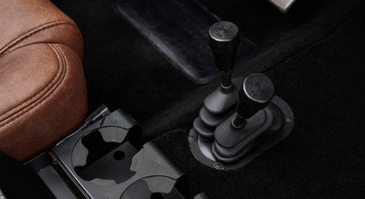 Two black gear shifters with manual shift pattern markings beside brown leather seat and cup holders