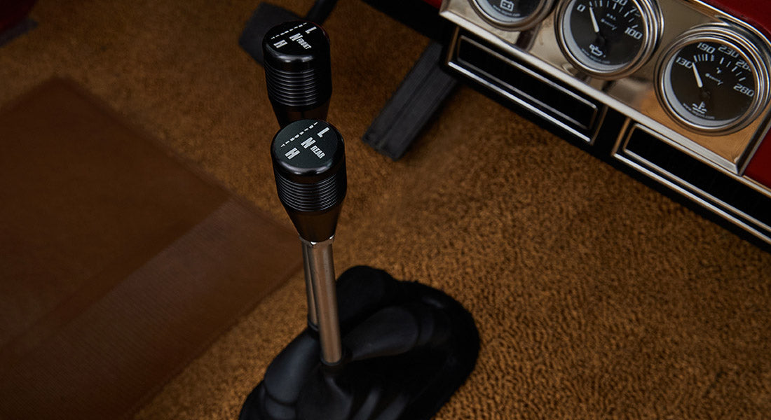 Two black gear shifters on tan carpet near Classic Ford Bronco dashboard gauges