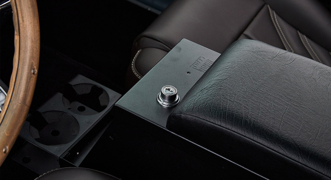 Black Tuffybox security console on center floor next to brown leather seat and wood rim steering wheel