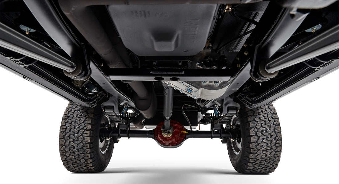 Undercarriage view of Classic Ford Bronco showing suspension, exhaust, and large off-road tires.