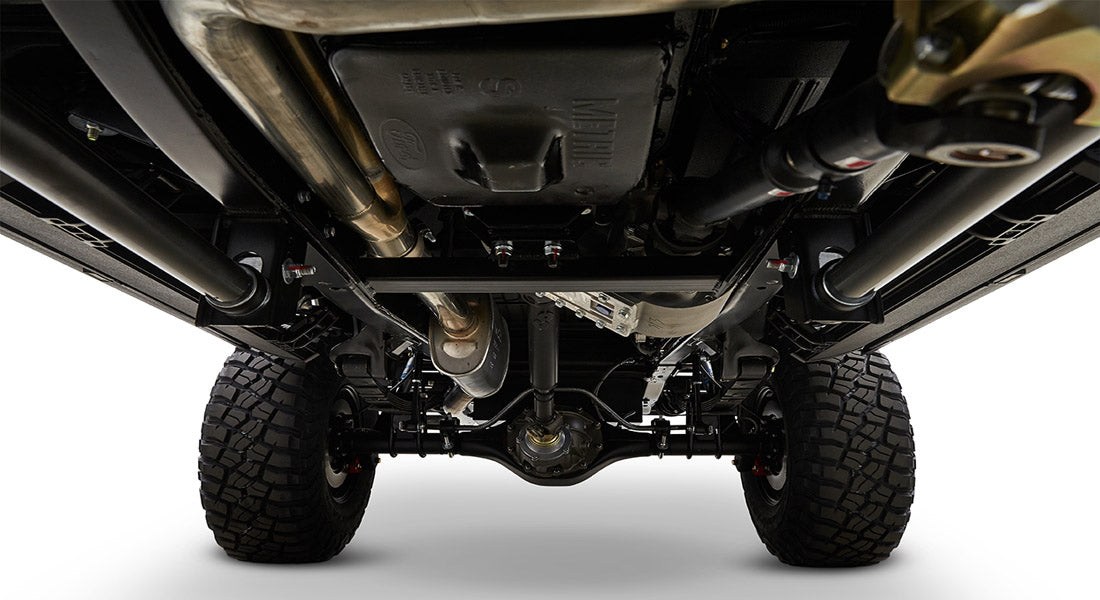 Undercarriage view with differential, suspension components, exhaust pipes, and off-road tires