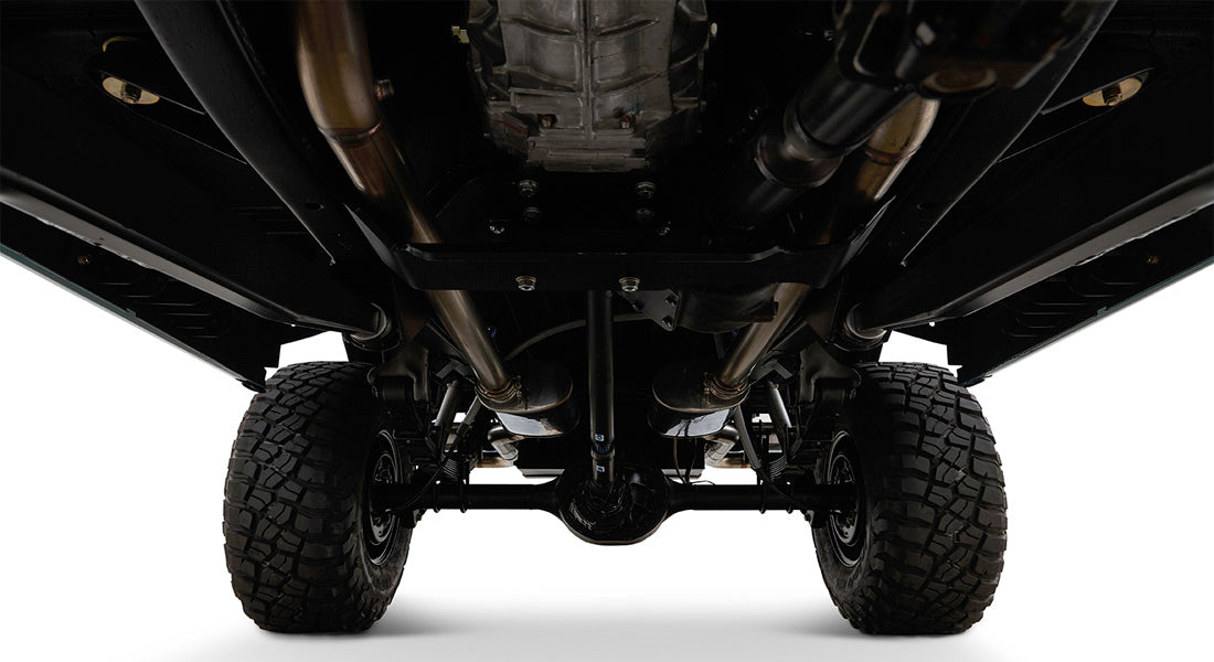 Undercarriage of a vehicle showing suspension, differential, and large off-road tires against a white background