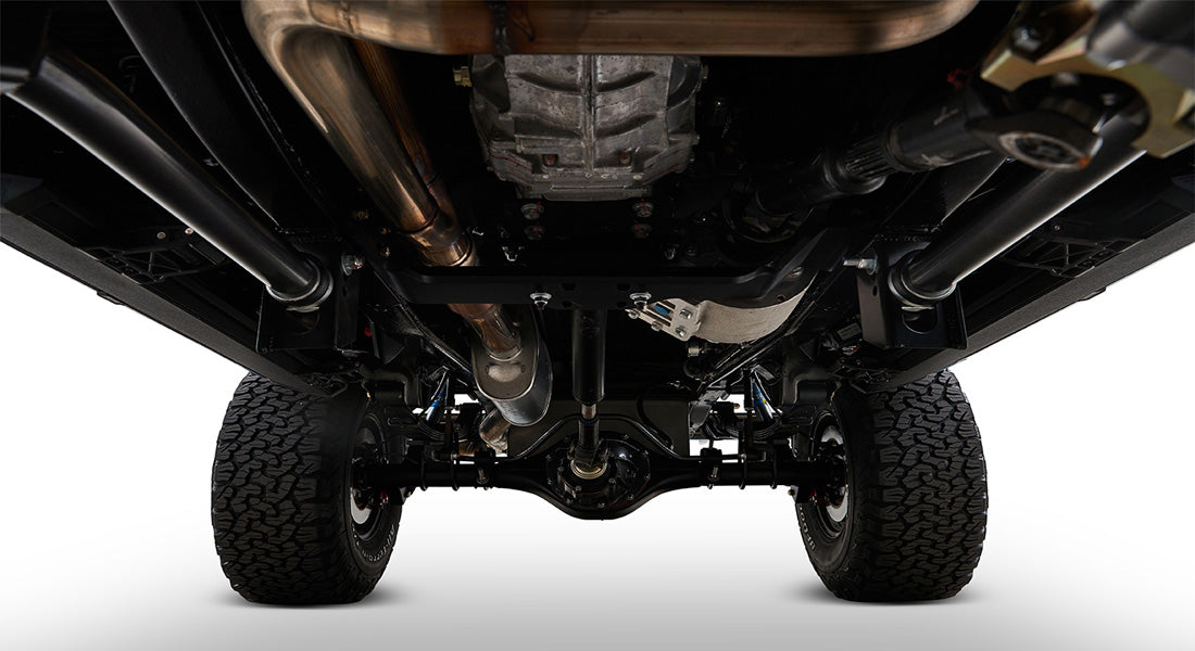 Black and silver undercarriage components including exhaust pipes and axles beneath a Classic Ford Bronco